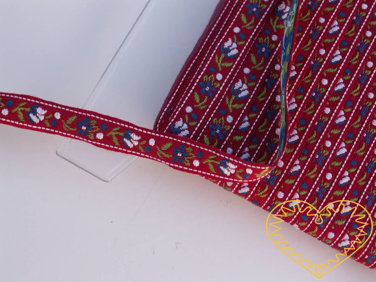 Úzká červená krojová stuha se vzorem - vzorovka - šíře 1 cm. Textilní tkaná stuha s jemným vzorkem je vhodná zvláště při výrobě krojů a předmětů tradiční lidové kultury. Vhodná též k lemování tkanin a šatů panenek a maňásků.